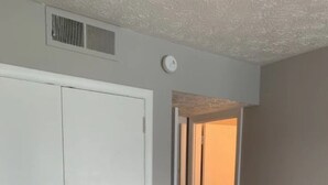 Een gang met een witte deur, een ventilatie rooster in het plafond en een klok.
