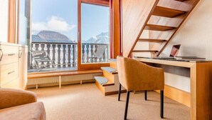 Ein modernes Zimmer mit großem Fenster, Schreibtisch, Stuhl und Treppe.