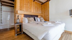 Ein Hotelzimmer mit Holzboden, einem großen Bett mit weißer Bettwäsche, einem Nachttisch mit Lampe sowie einem an der Wand befestigten Fernseher.