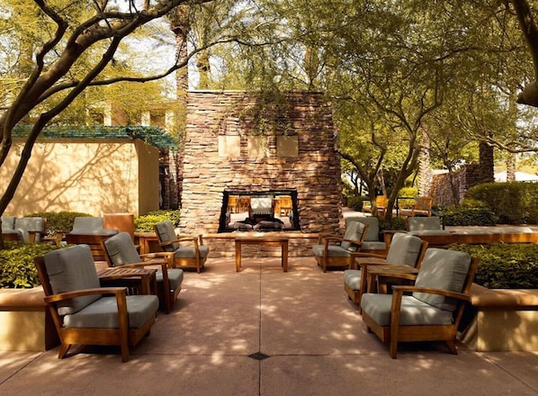 Relax by the stone fireplace in this serene outdoor seating area surrounded by comfortable chairs and tables.