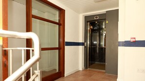 A hallway with a glass door, a metal handrail, and a tiled floor.
