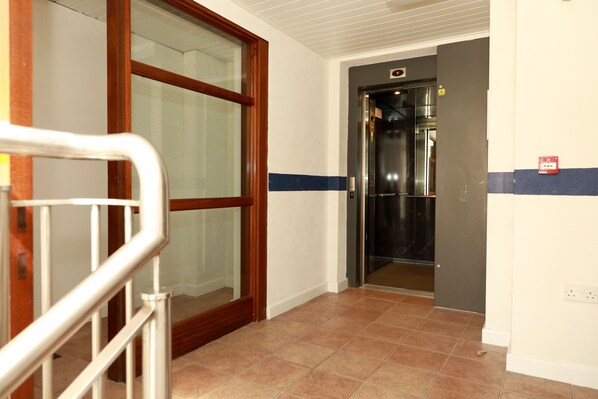 A hallway with a glass door, a metal handrail, and a tiled floor. - Sea View Apartment (Galway)