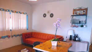 Ein Wohnzimmer mit Holztisch, zwei Stühlen, einem roten Sofa, einem kleinen runden Tisch mit Pflanze und einer Kommode mit Flaschen.
