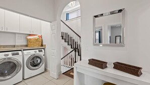 A laundry area with two washing machines, a white staircase, and a mirror on the wall. - Lake Norma Luxury Living - Coronas Azul (Siesta Key)