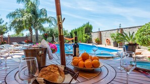 A poolside dining setup with a table, wine glasses, a bottle of wine, a basket of oranges, and a loaf of bread. - Villa Jeroma  Mijas Costa by Ruralidays (Málaga)
