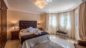 Un dormitorio elegante con una cama grande, una mesita de noche, una silla y una araña.