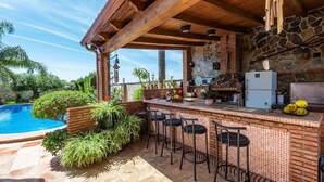 Un área de bar al aire libre con piscina, paredes de piedra y taburetes de bar.
