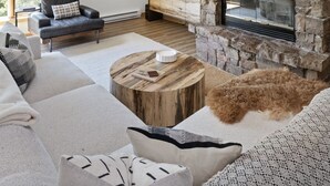 Un salon moderne doté d’une cheminée en pierre, d’un grand téléviseur à écran plat et d’un coin salon confortable avec un canapé en cuir et une table basse en bois.