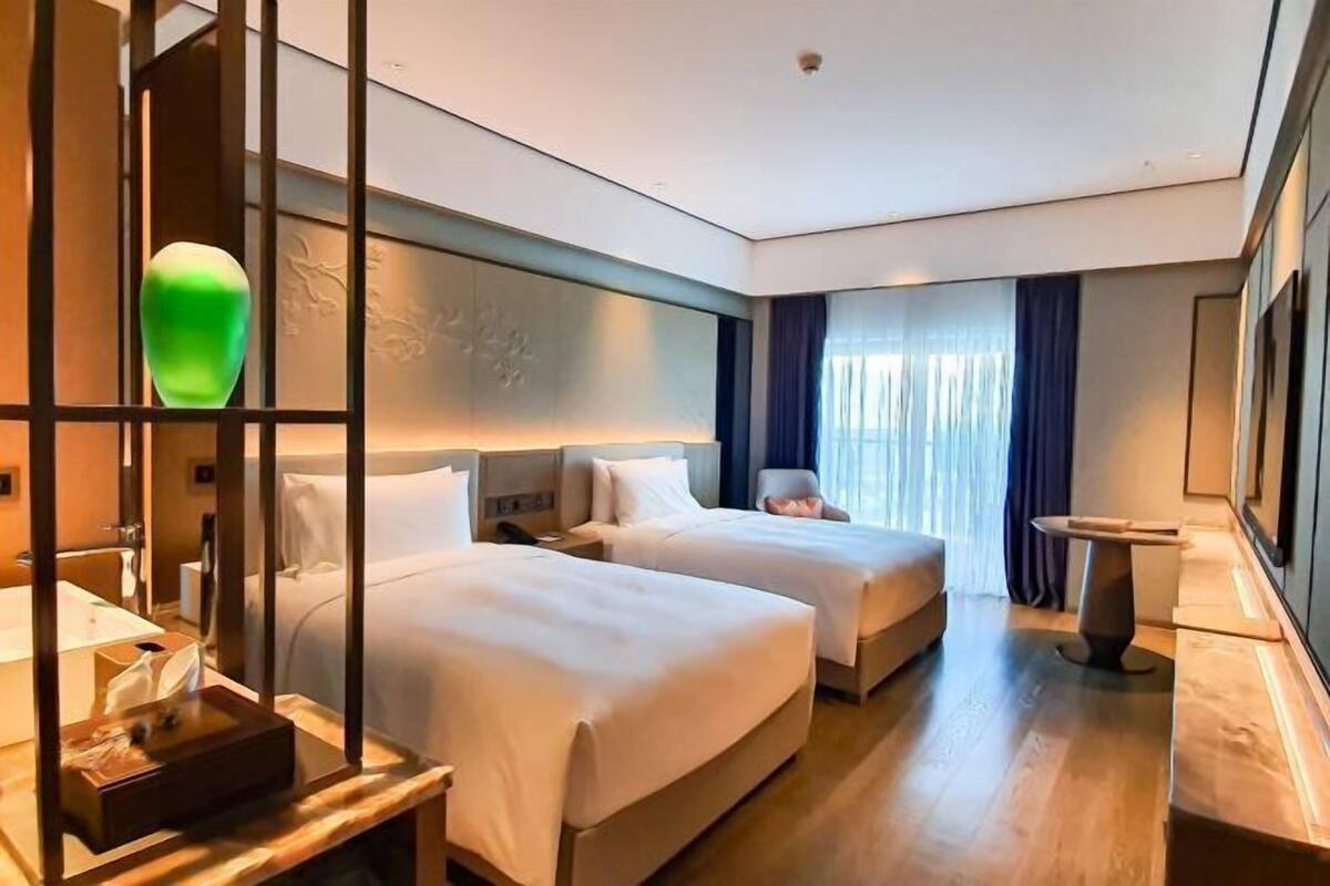Habitación de hotel con dos camas, un escritorio, una silla, una mesita de noche y un espejo grande.