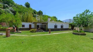Un edificio blanco con base de piedra, rodeado de un césped y jardín bien cuidados.