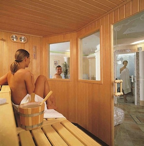 Una sala de sauna con paredes de madera y un banco. Hay un balde de madera con una cuchara sobre el banco.
