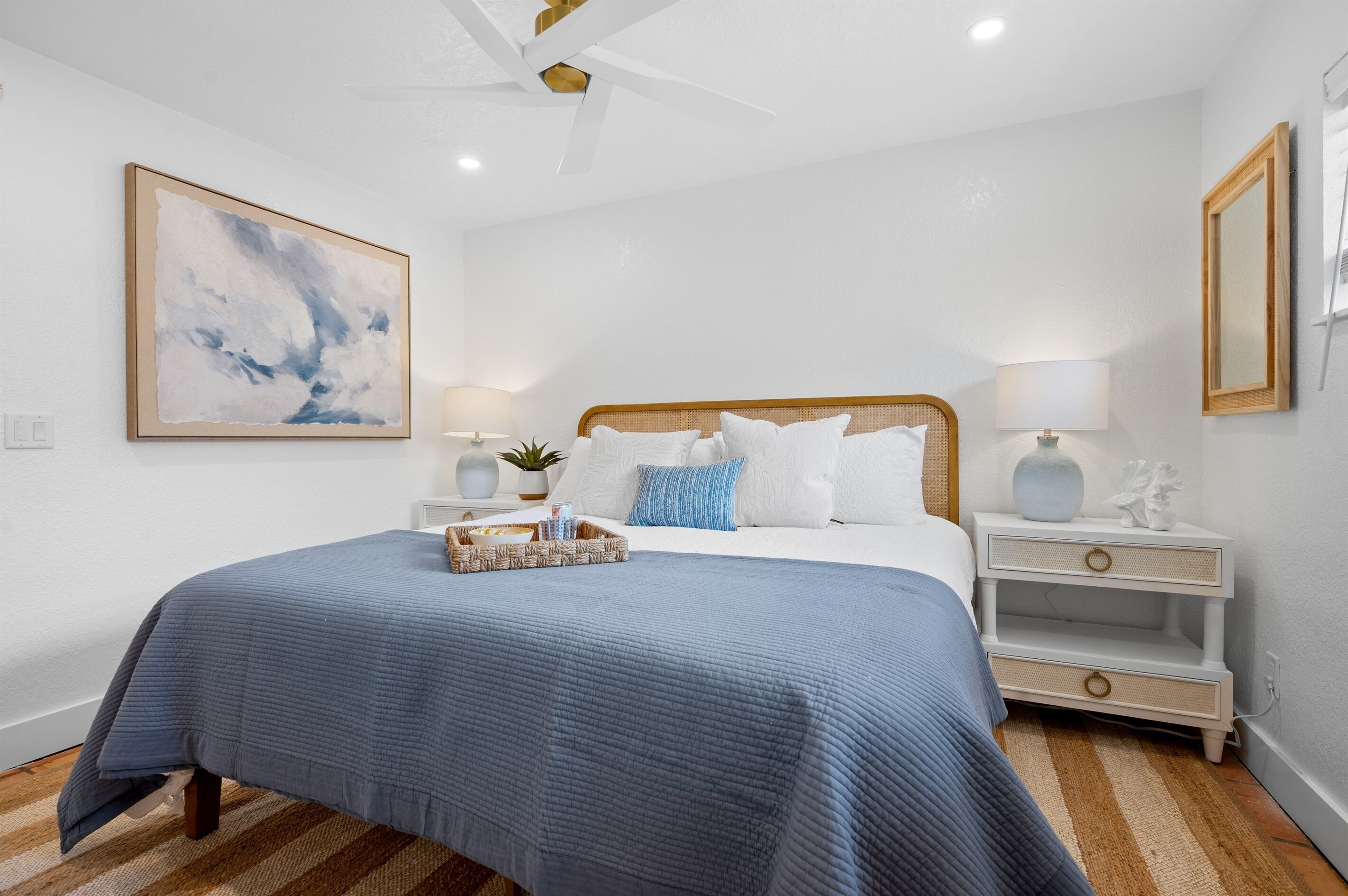 A neatly arranged bedroom with a large bed, bedside tables, a ceiling fan, and a wall-mounted mirror.