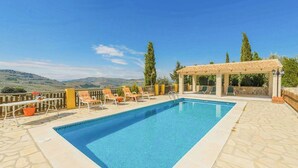 Una piscina rectangular con una pérgola y sillas de descanso en una terraza con vistas a la montaña.