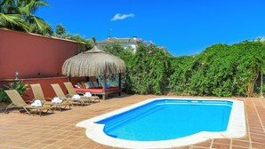 Una piscina con sillones de descanso y un área de estar con techo de paja.