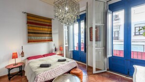 Una camera da letto con un letto, un lampadario, una porta rossa e vista sugli edifici esterni.