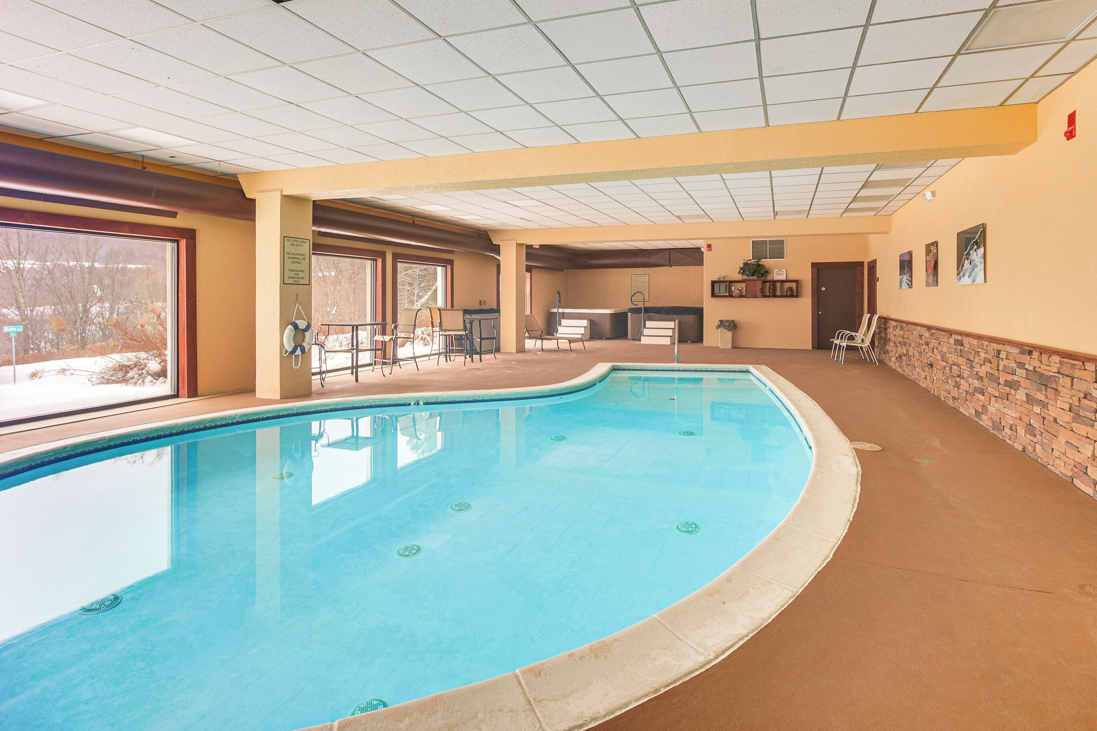 An indoor swimming pool with a tiled ceiling, a brick wall, and a door leading to another room.
