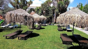 Relax in a serene outdoor space surrounded by lush greenery and shaded by thatched-roof structures.