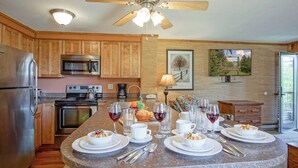 A kitchen with wooden cabinets, stainless steel appliances, a granite countertop, and a dining area set for six with wine glasses and plates. - Powderidge 1 Hideaway Slope Side (Snowshoe)