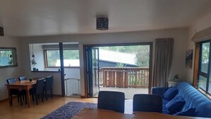 Een ruime woonkamer met een houten eettafel, een blauwe bank en uitzicht op het terras.