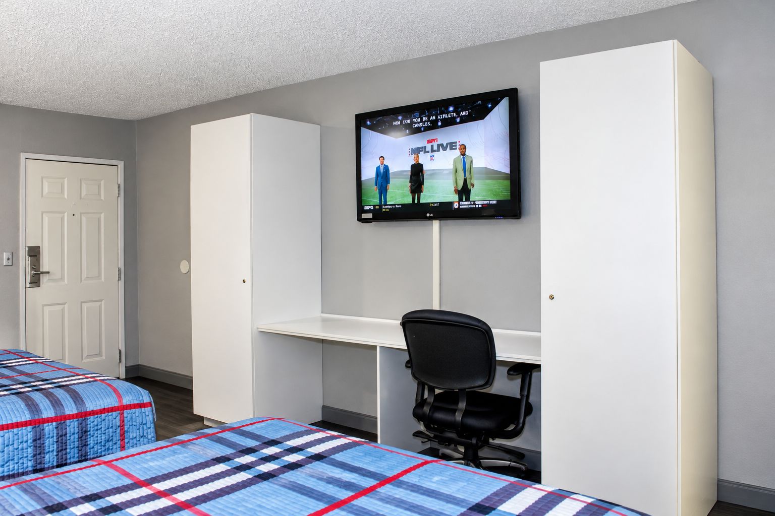 A hotel room with two beds, a desk, a chair, and a television mounted on the wall.