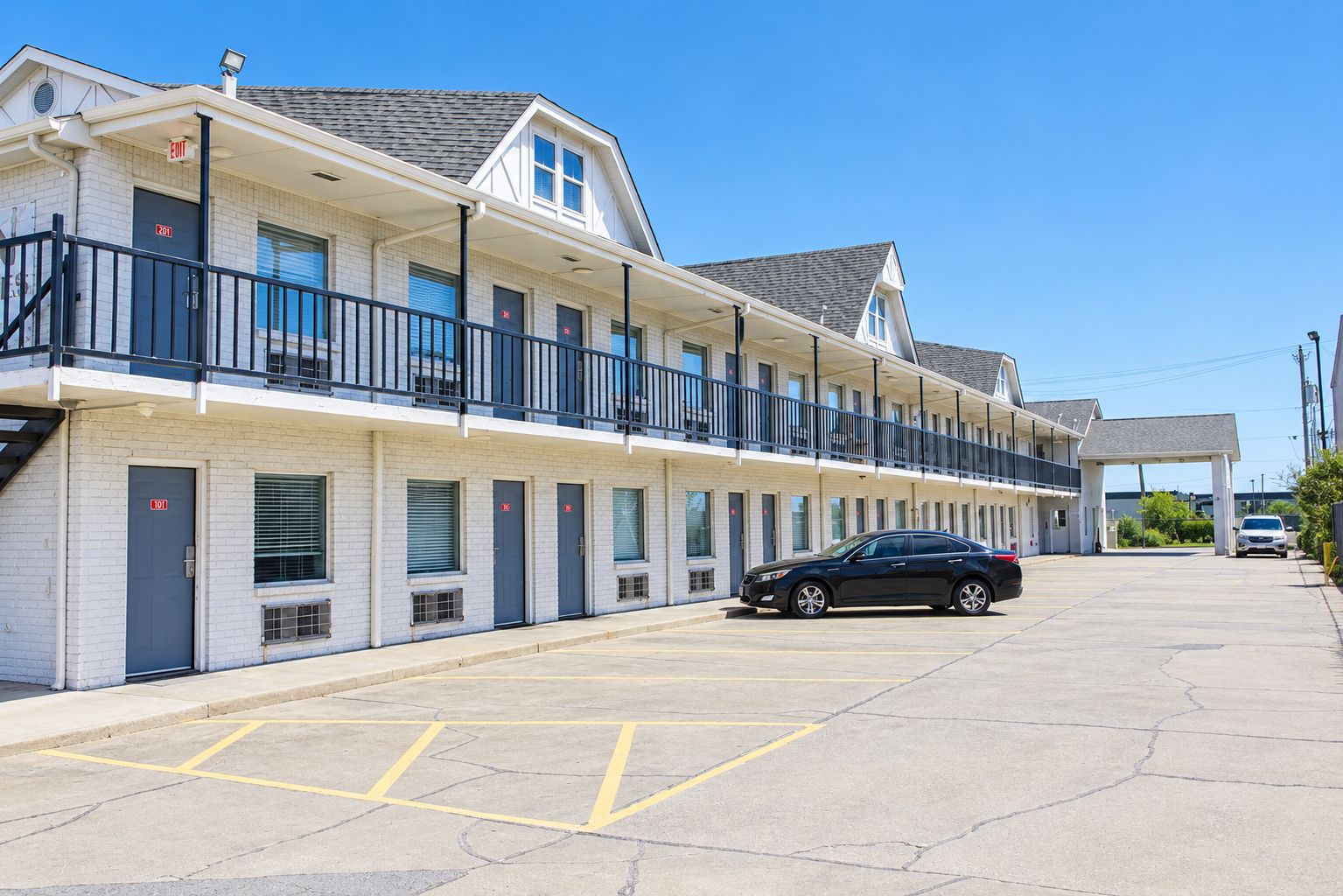 A motel with a row of rooms, a covered parking area, and a car parked in the lot.