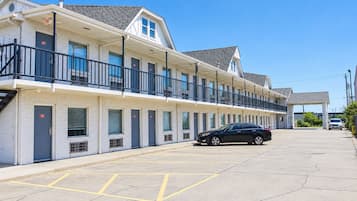 A motel with a row of rooms, a covered parking area, and a car parked in the lot.