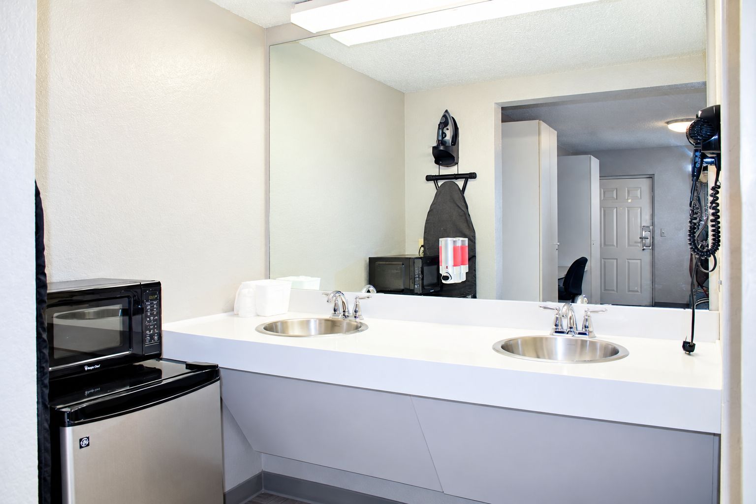 Un baño de hotel con lavamanos doble, un espejo, un microondas y un secador de pelo.