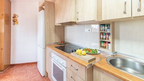 Et kompakt køkken med træskabe, en indbygget komfur, en vask og en lille bordplade med en salat.