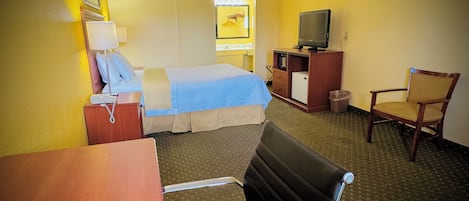 Una habitación de hotel con cama, escritorio, silla, televisor y refrigerador pequeño.