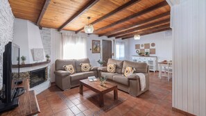 A living room with two sofas, a coffee table, a fireplace, a TV, and a kitchen area in the background. - Villa Jimena Nerja by Ruralidays (Málaga)