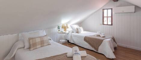 A room with two beds, a small table with a lamp, and an air conditioning unit on the wall.