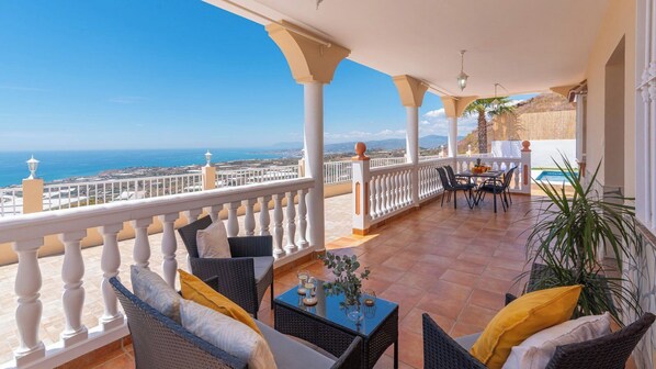 A covered terrace with wicker furniture, a table with drinks, and a view of the sea. - Villa Vista Vélez-Málaga by Ruralidays (Málaga)