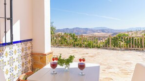 Une terrasse avec deux tables blanches, chacune agrémentée d’un verre de vin rouge et d’un petit vase de verdure.