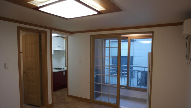 A room with a wooden floor, a sliding glass door leading to a balcony, and a ceiling light fixture.