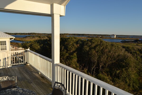 A wooden deck with a white railing overlooking a marshy landscape with water and trees.