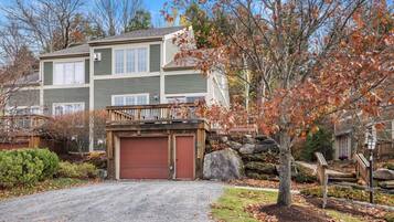 A two-story house with a garage, a wooden deck, and a stone wall.