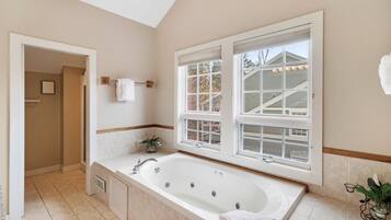 A bathroom with a large bathtub, two windows, a towel rack, and a potted plant.