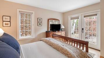 A bedroom with a bed, a dresser, a television, and two windows.
