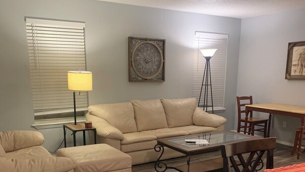 A living room with a beige sofa, a glass coffee table, a wooden dining table with chairs, and a floor lamp. - Furnished 1Bed 1Bath (Van)