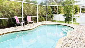 A pool area with a glass enclosure, two pink chairs, and a white fence in the background.