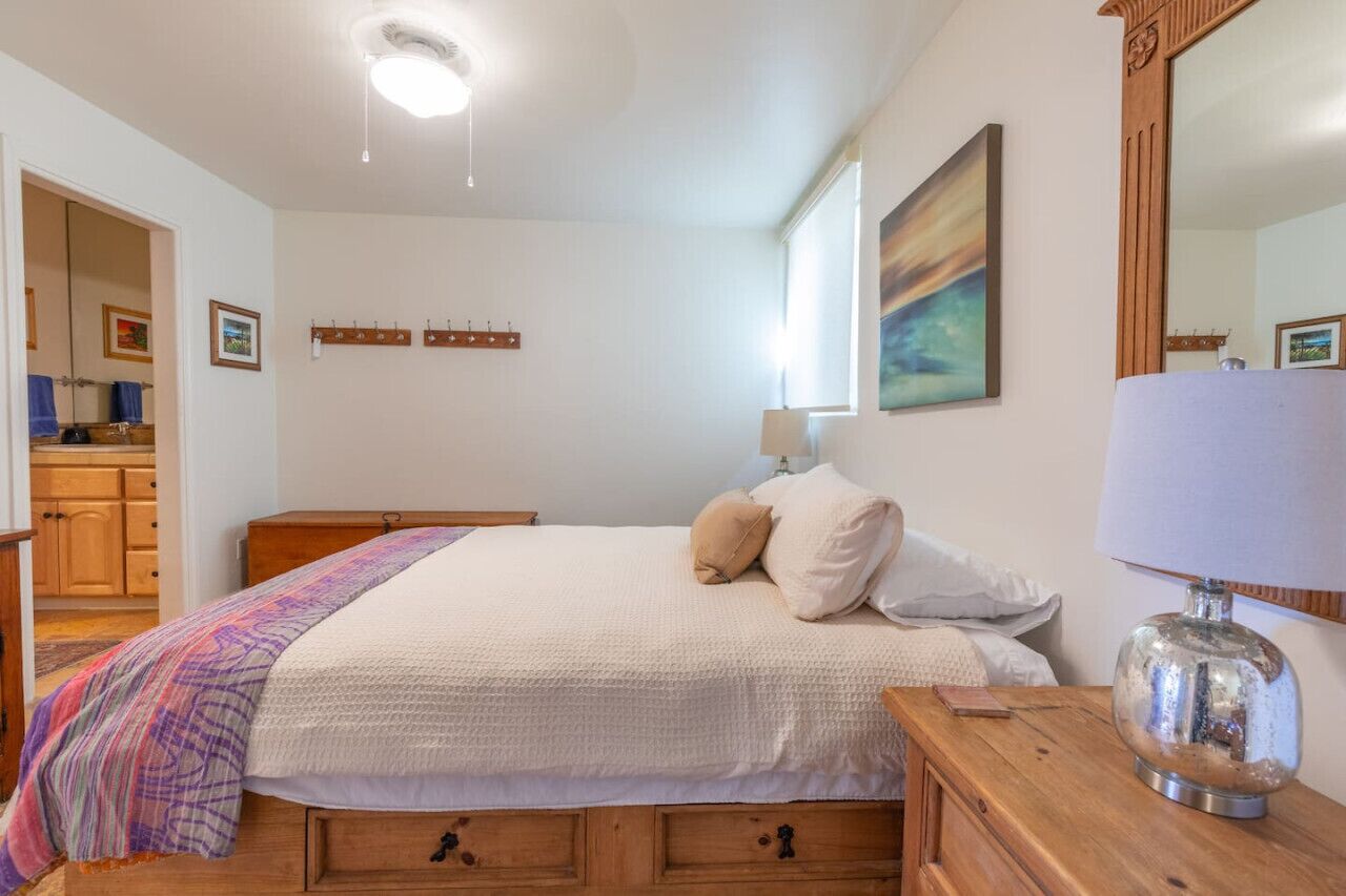 Un dormitorio con cama, mesitas de noche de madera, un espejo y un cuadro en la pared.