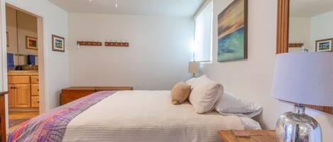 Un dormitorio con cama, mesitas de noche de madera, un espejo y un cuadro en la pared.