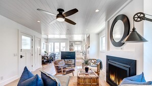 A spacious living room with a fireplace, a ceiling fan, and a large mirror. - Gorgeous 2-Level Condo | Rooftop Deck w/ Spectacular Views | Walk To It All | 5-Star Experience! (Newport Beach)