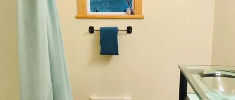A bathroom with a window, a towel rack, a glass shower enclosure, and a sink.