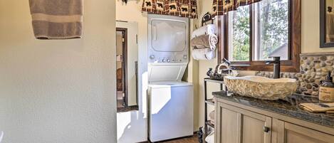 A laundry area with a washing machine, a sink with a stone basin, and a window with a plaid curtain.