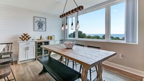 A modern kitchen with a wooden table, white cabinets, and a large window with a view. - Beautiful Beachfront Condo - Access to Amelia Island Golf & Beach Club (Fernandina Beach)