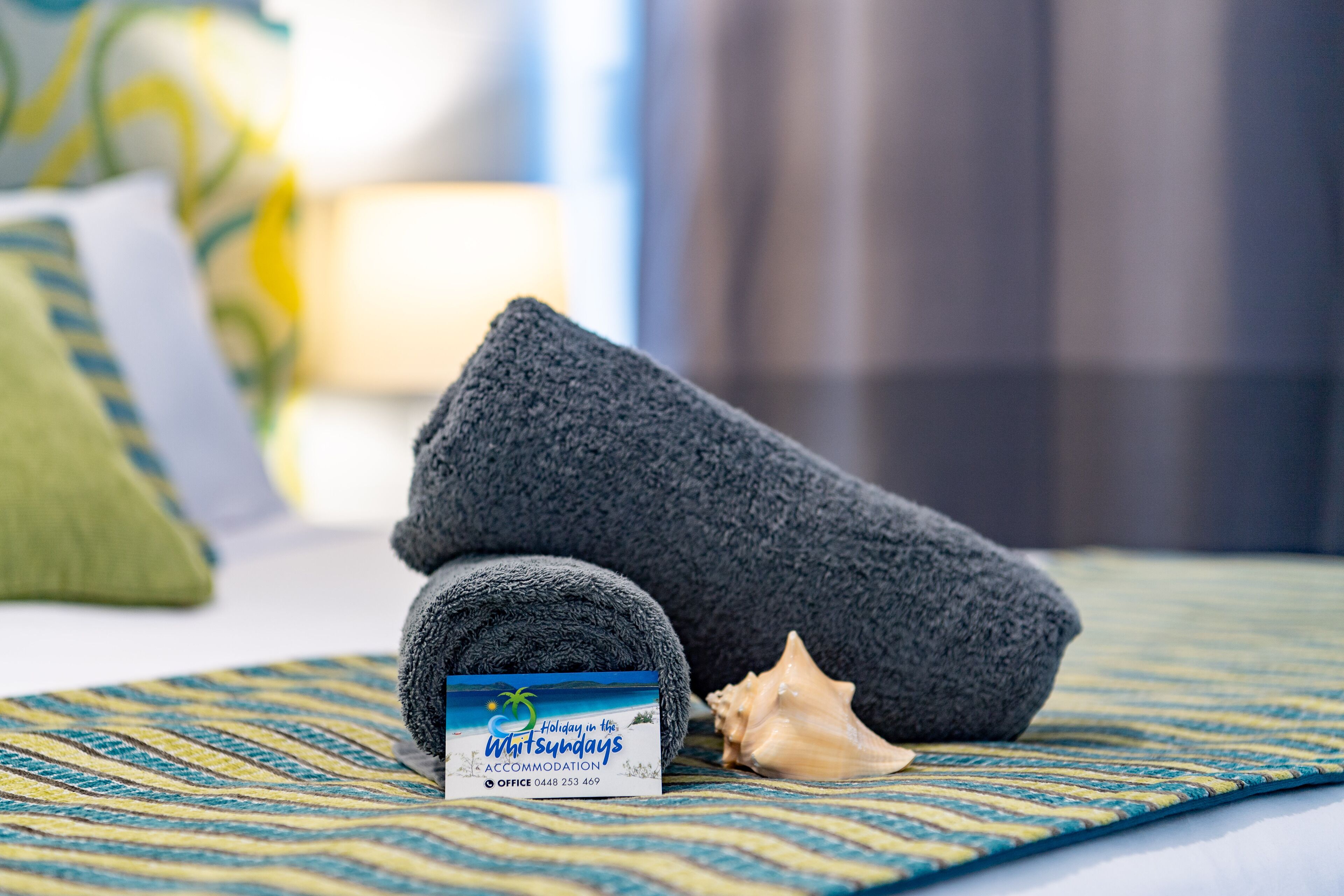 A neatly folded towel, a seashell, and a business card on a patterned bedspread.