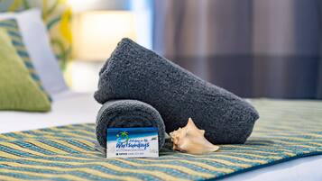 A neatly folded towel, a seashell, and a business card on a patterned bedspread.