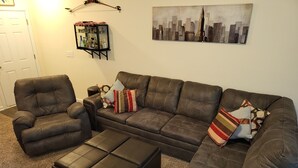 Un salon avec un canapé en cuir marron, un pouf assorti et un fauteuil en cuir. Un meuble vitré, contenant divers objets, est accroché au mur.