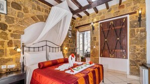 A stone-walled bedroom with a bed, a canopy, and a wooden door with decorative ironwork. - Cava Doro Hotel (Rhodes)